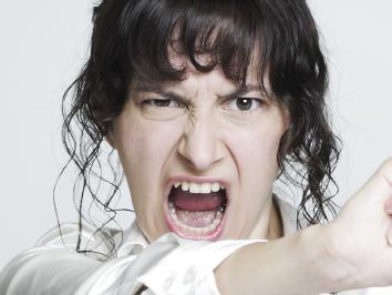 Young desperate woman at her paperwork-covered desk ripping up a tax form staring at the camera