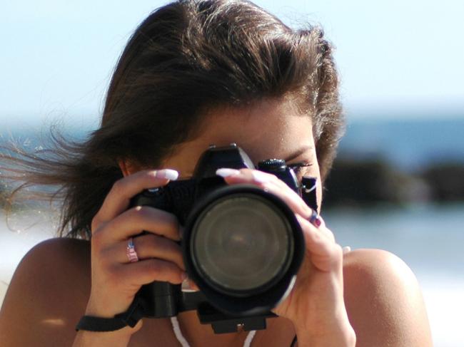 Young teen girl photographer looking through a DSLR camera lens while standing on the beach.