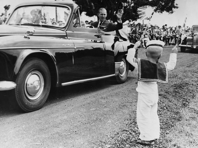 Seated beside Queen Elizabeth II, the Duke of Edinburgh waves to an enthusiastic little sailor, four-year-old Michael McCarthy during a tour of Mackay in Queensland. The royal couple attended a Children's Display and Reception at the Mackay Showground on March 16, 1954. Picture: Fox Photos/Getty Images