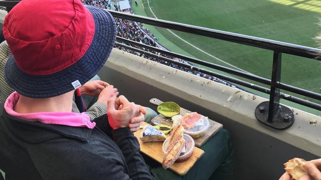 A Melbourne fan watches the footy with a cheese platter, including smashed avocado, on his lap. Pictures: Reddit user KrumDiddly