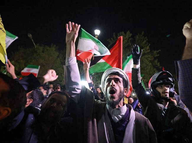 TOPSHOT - Demonstrators wave Iran's flag and Palestinian flags as they gather in front of the British Embassy in Tehran on April 14, 2024, after Iran launched a drone and missile attack on Israel. Iran's Revolutionary Guards confirmed early April 14, 2024 that a drone and missile attack was under way against Israel in retaliation for a deadly April 1 drone strike on its Damascus consulate. (Photo by ATTA KENARE / AFP)