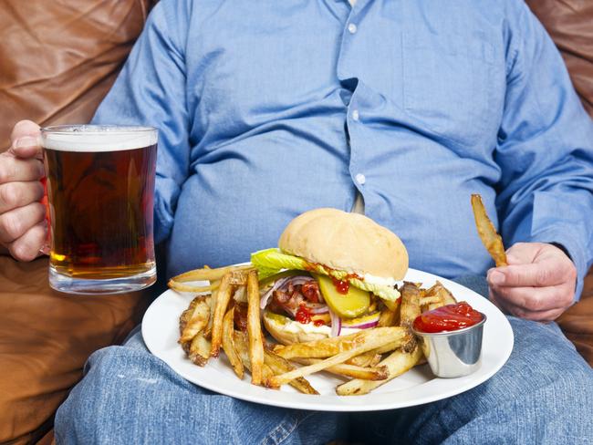 A photo of an overweight man sitting on an old couch with a very large unhealthy meal on his lap and a pint of beer in his hand. Obesity is a major cause of diabetes.