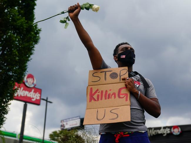 TOPSHOT - A man holds a sign and a white rose in his fist while facing traffic outside a burned Wendyâs restaurant on the second day following the police shooting death of Rayshard Brooks in the restaurant parking lot June 14, 2020, in Atlanta, Georgia. - The fatal shooting of a black man by a white police officer, this time in Atlanta, Georgia, poured more fuel June 14, 2020 on a raging US debate over racism after another round of street protests and the resignation of the city's police chief. A Wendy's restaurant where 27-year-old Rayshard Brooks was killed was set on fire June 13, 2020 and hundreds of people marched to protest the killing. (Photo by Elijah Nouvelage / AFP)