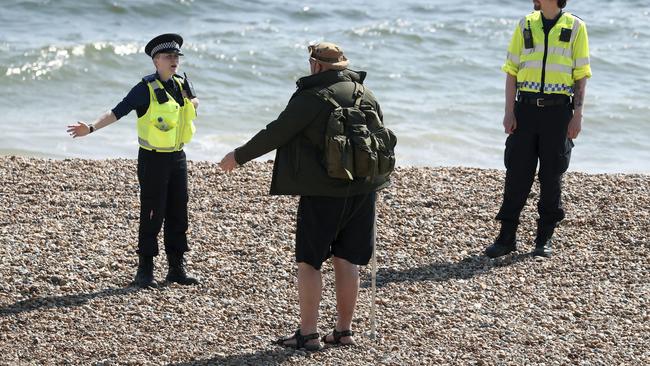 Police officers speak to a man as they patrol the beach in Brighton as the UK.