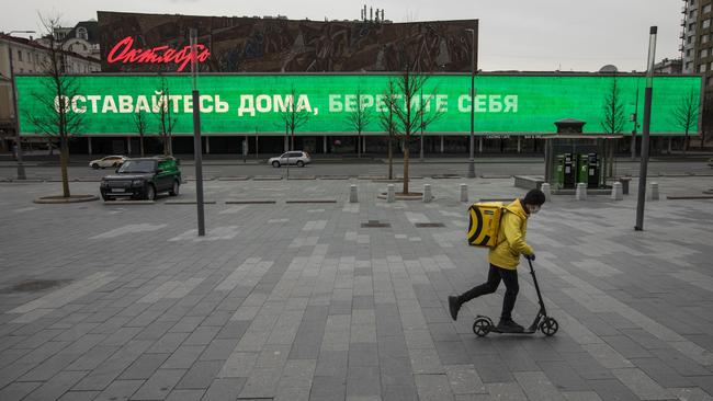 A food delivery courier rides a scooter in Moscow’s empty New Arbat Avenue, past a sign that reads “Stay home, take care of yourself”. Picture: AP