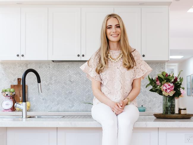 Portrait of a young blonde woman sitting on her kitchen benchtop at home