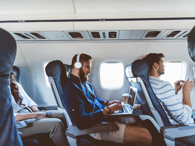 Young bearded man sitting inside an airplane and using a laptop. Male passenger using computer during flight. Picture: iStockTravel tech, Escape, jennifer Dudley Nicholson