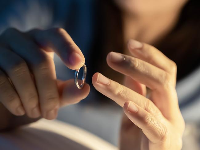 Divorce concept - close up of asian sad depressed woman taking off her wedding ring on the bed