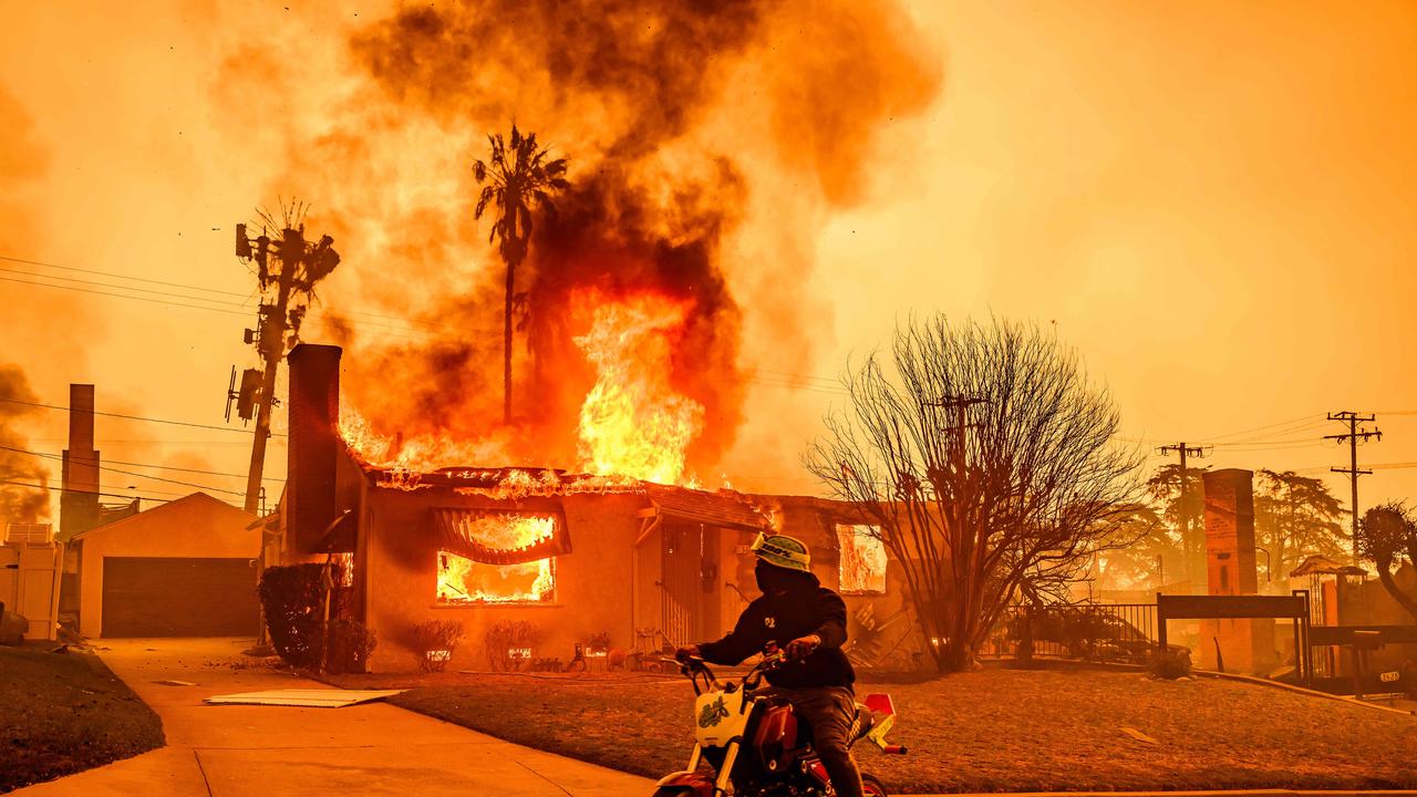 A motorcyclist stops to look at a burning home during the Eaton fire. (Photo by JOSH EDELSON / AFP)