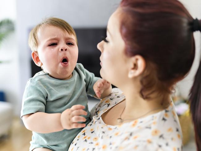 A mother holding child baby on the living room. The baby is sick having some cough. Istock Photo