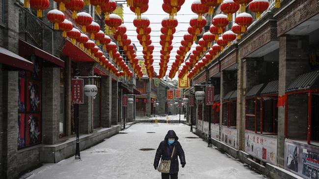 A Chinese woman wears a protective mask as she walks during a snowfall in an empty street in Beijing, China. Photo: Kevin Frayer, Getty Images.