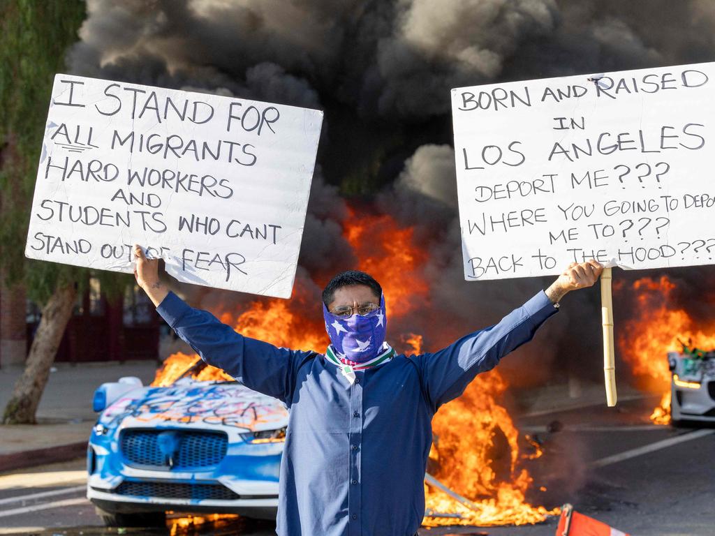 A man holds signs as cars burn in Los Angeles. Picture: AFP