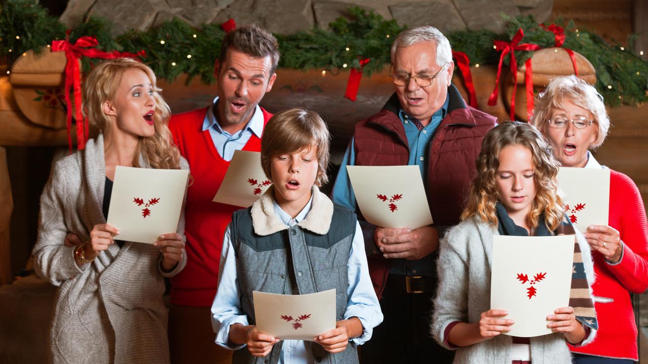 Multiple generations of one family sing carols in front of their fireplace.
