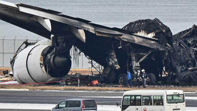 Officials look at the burnt wreckage of a Japan Airlines passenger plane on the tarmac. Picture: AFP