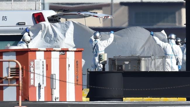 Workers in protective gear hold up a sheet as a passenger is transferred into a waiting ambulance in Yokohama, Japan. Picture: Kazuhiro NOGI, AFP