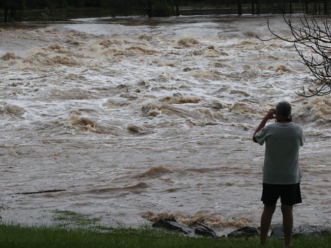 People gather to watch floodwaters in the Coomera River spill over the Oxenford Weir. Picture Glenn hampson