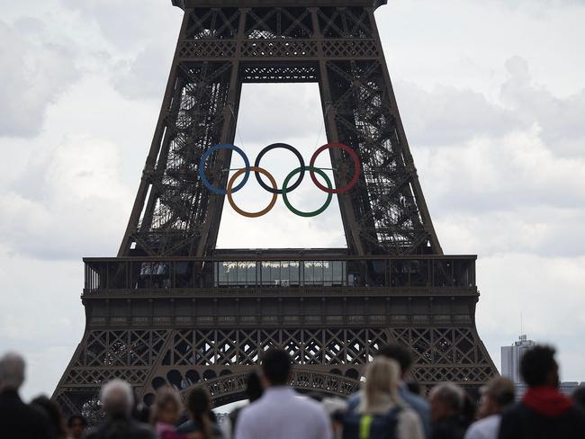 (FILES) People stand in front of the Eiffel Tower, decorated with the Olympic rings for the upcoming Paris 2024 Olympic Games, in Paris on June 14, 2024. As of today, the adult ticket price to ride the lift to the top of the Eiffel tower, is 35.30 euros (37.77 USD) compared to the 29.40 euro (31.90 USD) that visitors used to pay to climb one of the world's most famous monuments, in Paris, on June 17, 2024. (Photo by Valentine CHAPUIS / AFP)