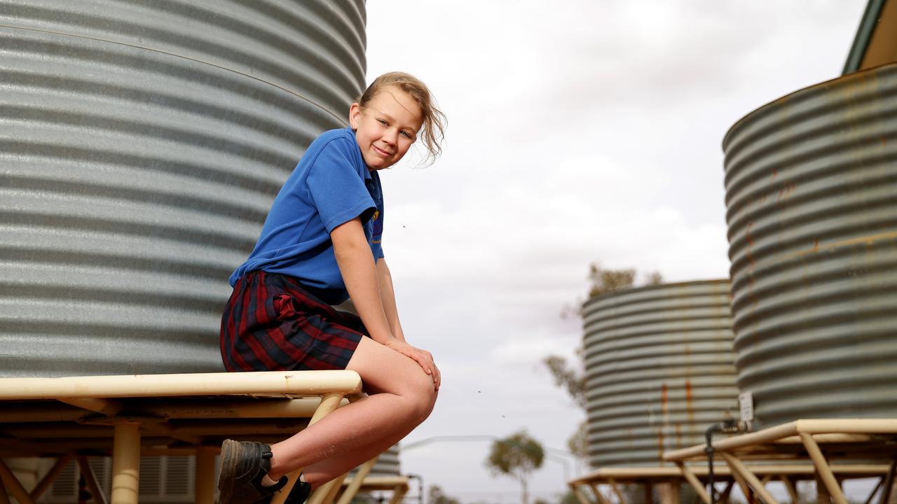 Hermidale Public School’s Jade Thompson, 11, with some of the schools rain water tanks. Picture: Jonathan Ng