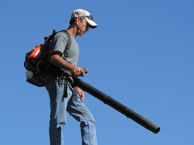 A man uses a high-powered air blower against a sunny blue sky.