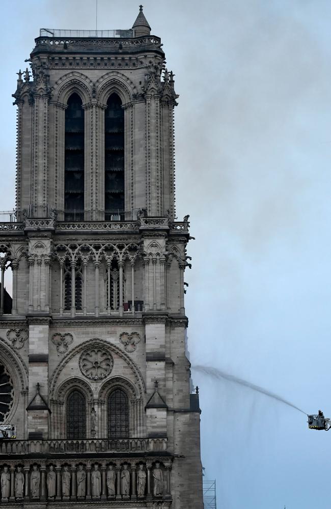 A fire fighter is seen dousing the facade of the Notre-Dame de Paris Cathedral as flames engulf the roof of the cathedral on April 15, 2019, in the French capital Paris. (Photo by STEPHANE DE SAKUTIN / AFP)