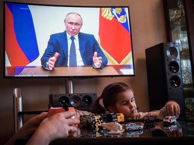 A woman watches a live broadcast of Russian President Vladimir Putin’s address to the nation over the coronavirus outbreak as her daughter plays with toys in her Moscow apartment. Picture: AFP