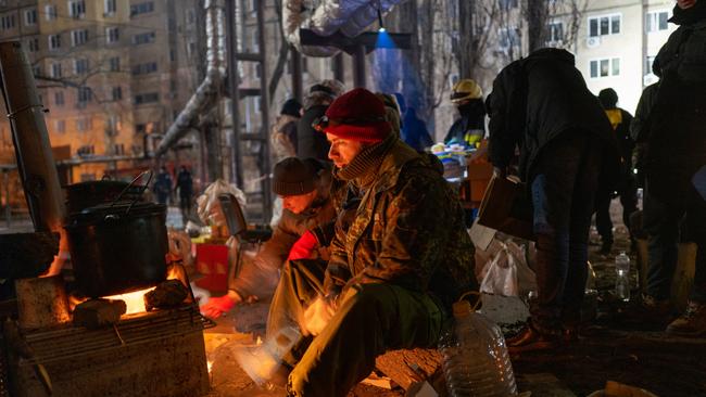 People stay warm as emergency workers search the remains of a residential building that was struck by a Russian missile in Dnipro, Ukraine. Picture: Getty Images