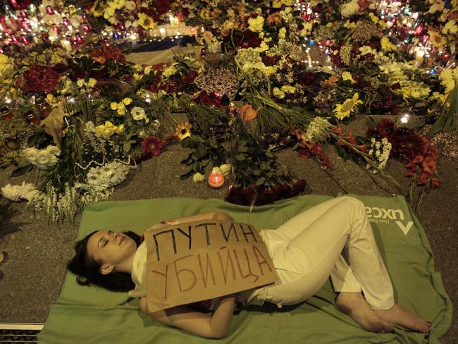 Ukrainian woman lies down in front of Dutch embassy holding a poster reading “Putin is a killer”. AP Photo/Sergei Chuzavkov