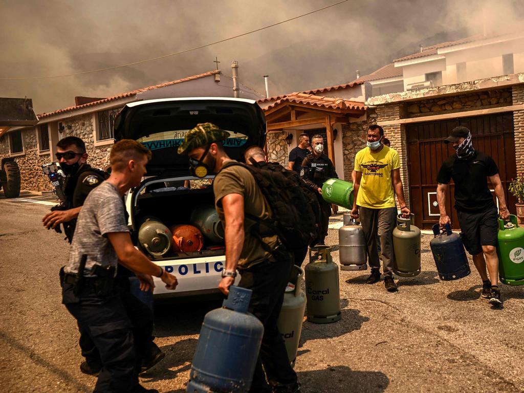 Police officers and volunteers clear bottled gas as a wildfire spreads in Acharnes, north of Athens. Picture: Angelos Tzortzinis / AFP