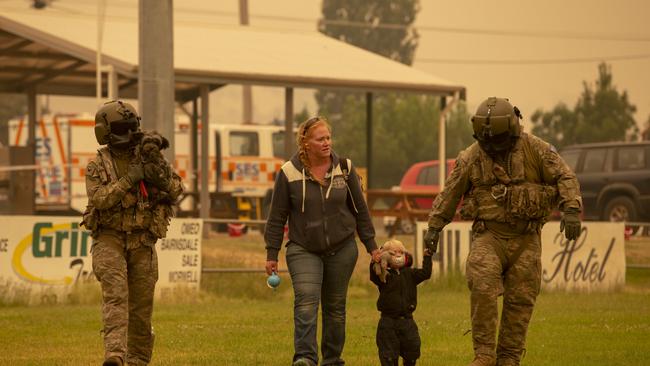 Two Australian Army Soldiers help people evacuate onto a helicopter/