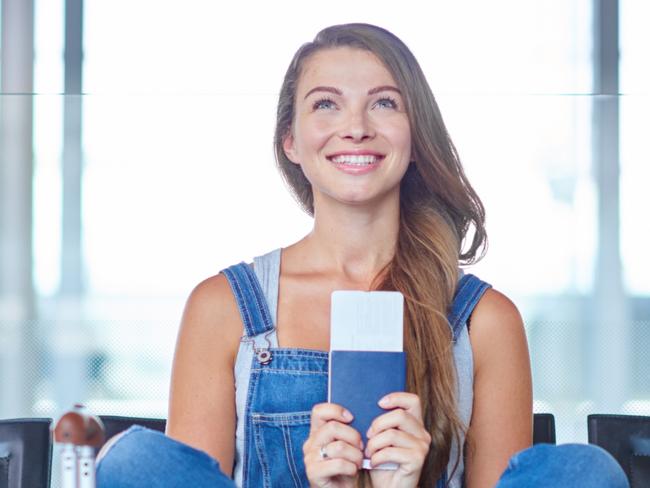 ESCAPE. JAN 9, 2022. Shot of a young woman holding her passport and ticket while sitting on a chair in an airport departure lounge. Picture: iStock