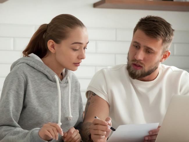 Focused young couple checking analyzing utilities bills sitting together at kitchen table, serious husband and wife reading bank loan documents with laptop, family managing finances planning expenses; money generic