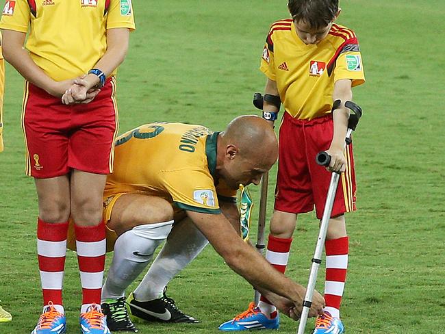 Australia V's Chile at Arena Pantanal, Group B in the 2014 World Cup, 13th June, Cuiaba, Brazil. Australia's Mark Bresciano comes out with a boy on crutches and help him tie up his shoe laces. Pic : George Salpigtidis