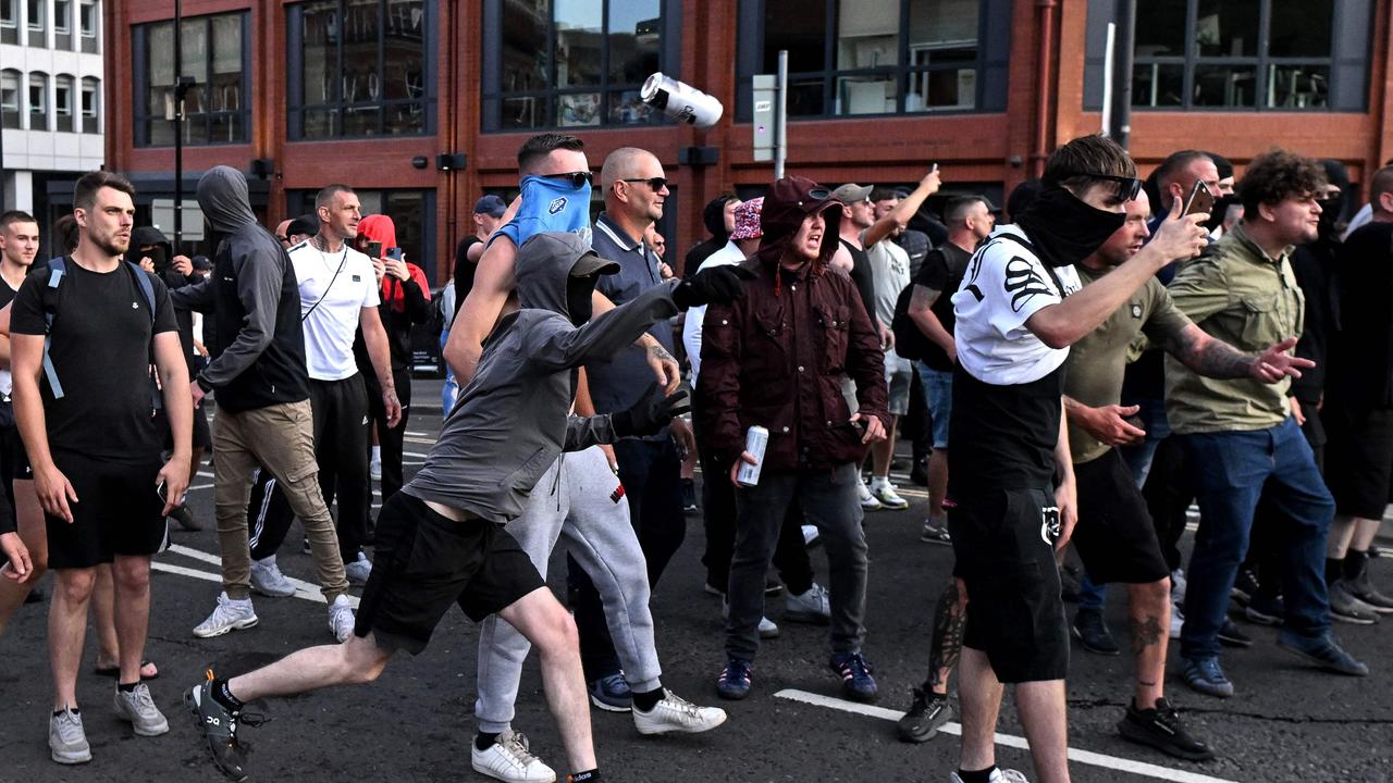 A masked protester throws a can of beer towards riot police in Bristol, southern England, on August 3, following a mass stabbing that killed three young girls. (Photo by JUSTIN TALLIS / AFP)