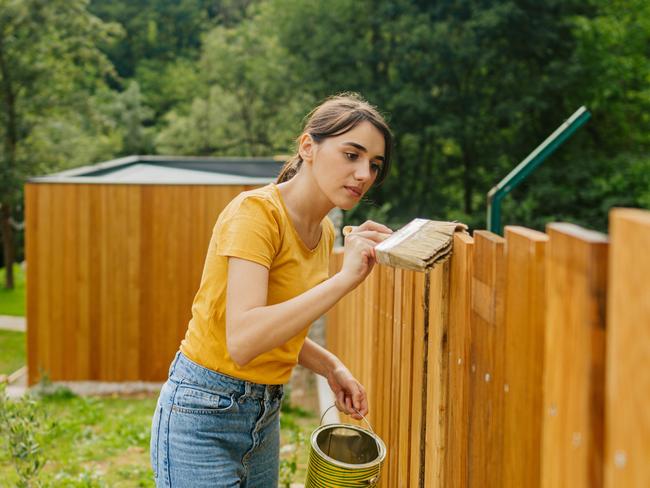 CAREERS: One side hustle is no longer enough to make ends meet, with a growing number of Australians requiring several income streams to pay their mortgage and put food on the table.  Photo of a young woman painting a garden fence. Picture: iStock