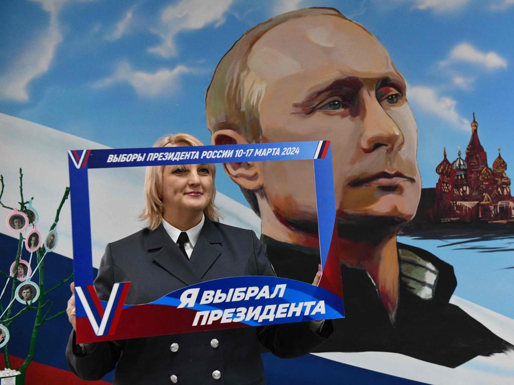 A woman poses with a frame reading "I chose a president" in front of a mural depicting Russian President Vladimir Putin during Russia's presidential election. Picture: AFP