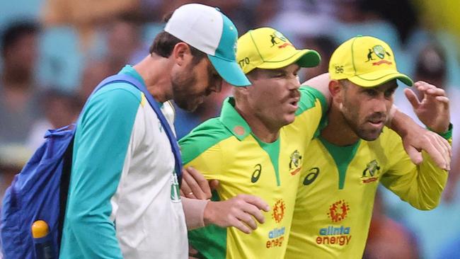 Australia's David Warner (C) is assisted by teammate Glenn Maxwell (R) and a trainer as he leaves the field after he suffered an injury during the one-day cricket match against India at the Sydney Cricket Ground (SCG) in Sydney on November 29, 2020. (Photo by DAVID GRAY / AFP) / — IMAGE RESTRICTED TO EDITORIAL USE – STRICTLY NO COMMERCIAL USE —