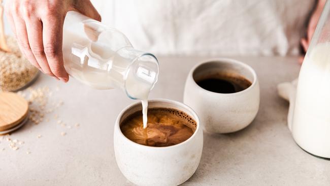 Close-up of pouring oat milk into black coffee cup. Making coffee at home.