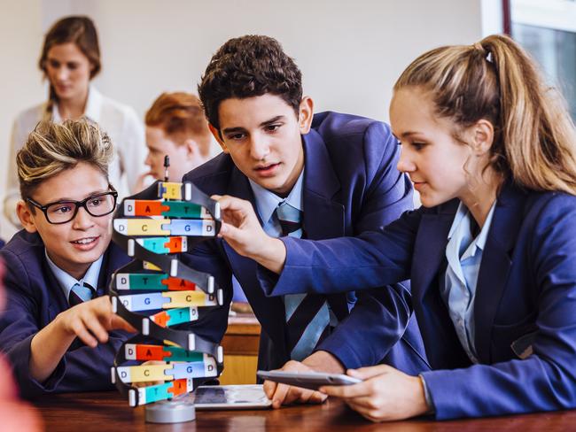 Class of young teenagers with their female teacher sat at a table in the science lab using a helix model. The children are wearing school uniform. Picture: iStock