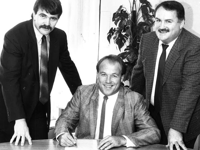 Wally Lewis signs on for the Broncos as CEO John Ribot (left) and the Maranta Consortium’s Gary Balkin look on.