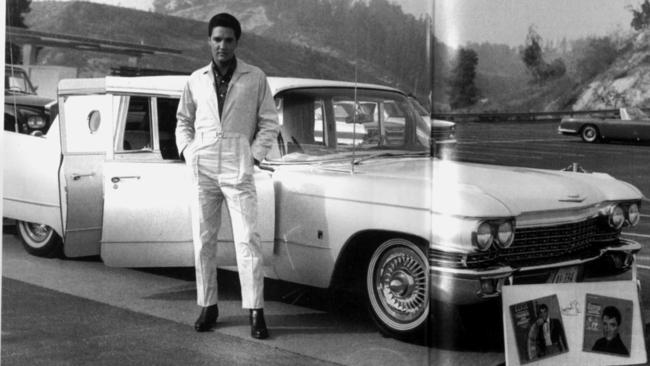 Elvis Presley standing next to a nice set of wheels.