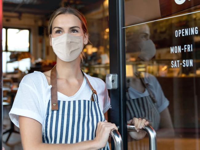 Happy business owner opening the door at a cafe wearing a facemask to avoid the spread of coronavirus â reopening after COVID-19 concepts