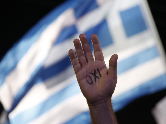 FILE - In this July 3, 2015 file photo, a demonstrator raises his hand with the word ''No'' written on it as a Greek flag waves behind during a rally organized by supporters of the No vote in Athens. From Grexit to Grimbo, Greece’s debt crisis has spawned its own awkward argot. (AP Photo/Petros Giannakouris, File)