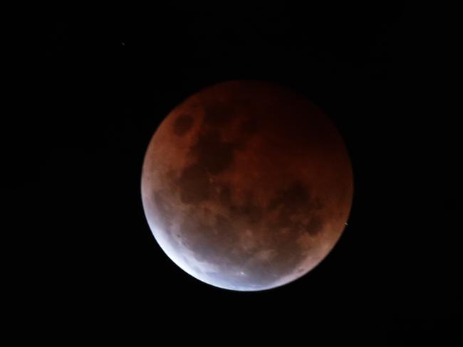 During a break in the clouds, the lunar eclipse is seen in the skies over Sydney, NSW Australia. Picture: Bill Hearne