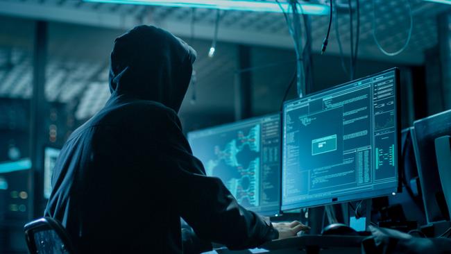 Shot from the Back to Hooded Hacker Breaking into Corporate Data Servers from His Underground Hideout. Place Has Dark Atmosphere, Multiple Displays, Cables Everywhere; scams, scammer generic