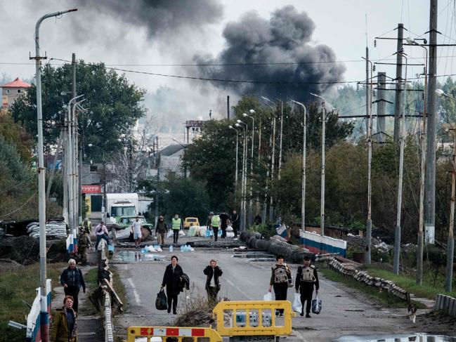 TOPSHOT - A woman (3rd R), evacuating with belongings, protects her ears after an explosion on a bridge over the Oskil River as black smoke rises in the frontline city of Kupiansk, Kharkiv region, on September 24, 2022, amid the Russian invasion of Ukraine. - In the northeastern town of Kupiansk, which was recaptured by Ukrainian forces, clashes continued with the Russian army entrenched on the eastern side of the Oskil River. (Photo by Yasuyoshi CHIBA / AFP)