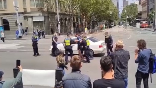 A man standing on a car with a crossbow outside state parliament.