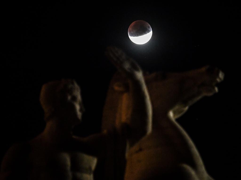 The moon is seen above a statue of "Palazzo della civilta del lavoro" or "Square Colosseum" in the EUR district , during a lunar eclipse in the sky over Rome, on July 16, 2019. (Photo by Andreas SOLARO / AFP)