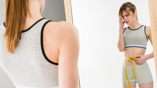 young depressed woman measuring her waist and looking at mirror isolated on white