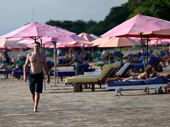 A foreign tourist walks on a beach in Seminyak, Badung regency on Indonesia resort island of Bali, on December 7, 2022. (Photo by SONNY TUMBELAKA / AFP)