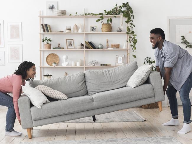 Happy african american couple moving sofa in living room, replacing furniture at home, side view